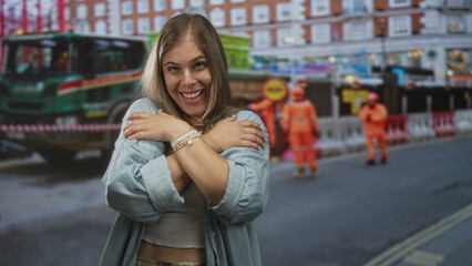 Fototapeta premium Woman smiling crosses arms across chest revealing bare belly on street under bright daylight; self acceptance.