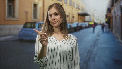 Young woman wearing a striped shirt rests hand on chin on street lined with parked cars and old...