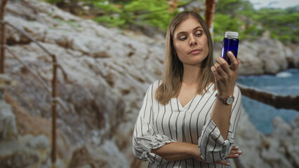 Woman holds glass bottle with raised hand in forest clearing examining it; curiosity inquiry evaluation.