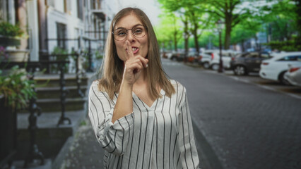 Fototapeta premium Woman young blonde points finger to the right on a tree lined city street in striped blouse; playful surprise.