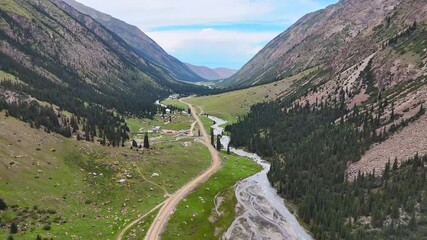 Drone video flying straight through Barskoon Gorge in Kyrgyzstan. Below, cars move along a gravel road, a river flows beside them, and ahead small mountain buildings. - Powered by Adobe