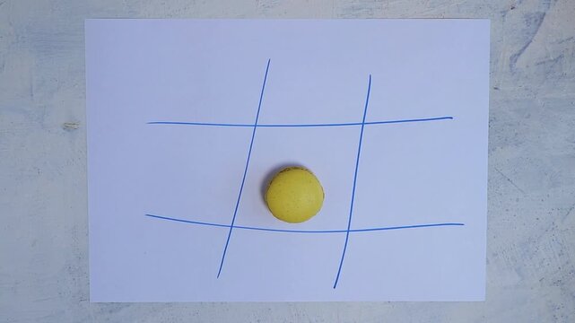 Top-down view of female hands playing tic tac toe with macarons and Oreo cookies on a hand-drawn paper grid. Static camera, fun and creative setup.