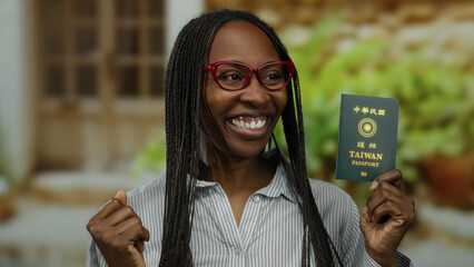 Woman holding taiwan passport outdoors in urban setting with joyful expression wearing red glasses...