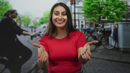 Woman with open palms offering gesture on street with bicycles and cobblestone, smiling broadly and...