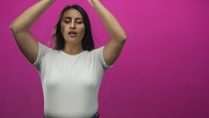 Woman with closed eyes and arms raised facing camera in studio against vivid magenta wall; serenity...