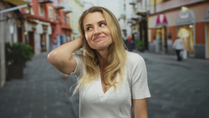 Fototapeta premium Woman outdoors on city street with blonde hair and casual white top expressing frustration, surrounded by urban environment, conveying emotion and lifestyle.