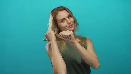 Woman smiling with thumbs pointing backwards against a vibrant green background captures youthful energy, charm, and positivity in an isolated setting.