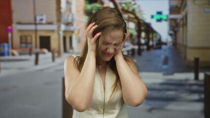 Woman in a white sleeveless top clenches fists and snarls on a sunlit city street lined with storefronts; anger.