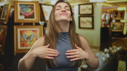 Fototapeta premium Woman smiles with closed eyes and moves hands before colorful paintings in a building; serenity and wonder.