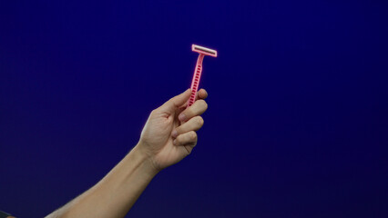 Man hand holding pink razor isolated over blue background.