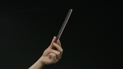 Caucasian man holding a black nail file against a dark background, showcasing a hand with a focus...