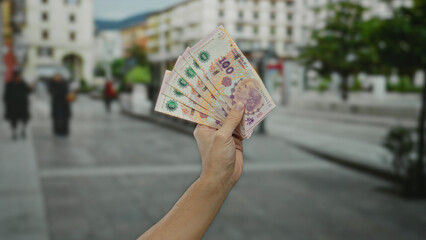 Man holding argentine pesos outdoors on a city street showcasing currency and finance in an urban...