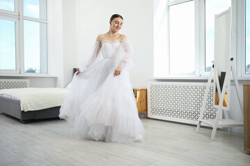 Dreams come true. Woman wearing beautiful wedding dress looking at herself in mirror indoors