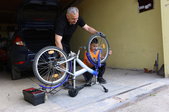 A man and a boy repair a bicycle together in the garage, fixing the wheel and learning teamwork, patience, and practical skills. - Powered by Adobe