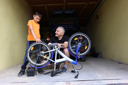 A man and a boy repair a bicycle together in the garage, fixing the wheel and learning teamwork, patience, and practical skills.