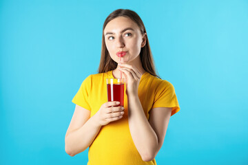 Woman drinking juice through straw on light blue background