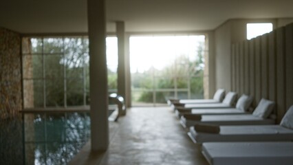 Defocused view of serene spa area with modern lounge chairs and large windows creating a tranquil ambiance for relaxation with natural light and blurred outdoor scenery.