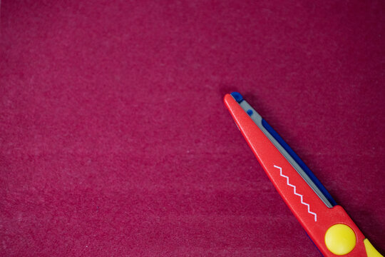 Red craft scissors with zigzag blade on pink textured background