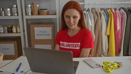 Woman volunteering at charity center with laptop surrounded by donations and clothing, highlighting...