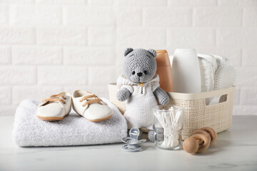 Many different baby accessories and toy bear on table near brick wall