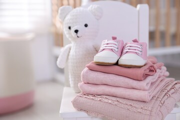 Stack of clean baby clothes, shoes and accessory on small chair indoors, closeup. Space for text