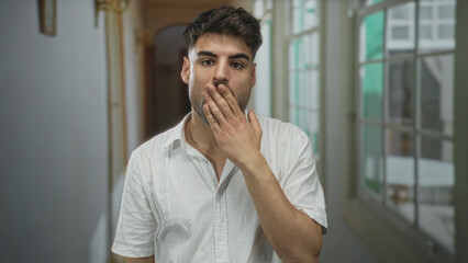 Man finger to lips for silence in hotel building corridor under soft daylight shining through...