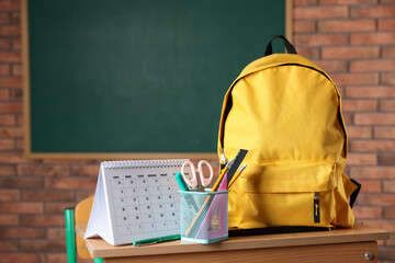 Yellow backpack, different stationery and calendar on desk in classroom