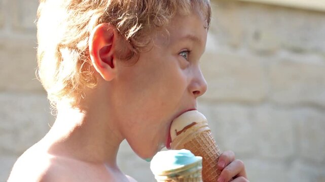 A little boy licking two ice creams