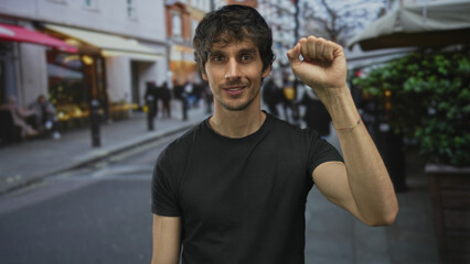 Man in black shirt raises clenched fist while looking at camera on busy city street amid blurred...