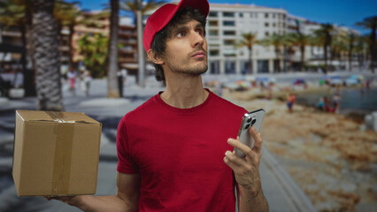 Man in red shirt holds package, scrolls smartphone and tilts head upward on street; anticipation...