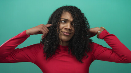 Woman wearing red shirt covers her ears with both hands and grimaces in studio; annoyance...