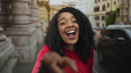 African american woman smiling and pointing finger at camera on city street in daylight; confidence...