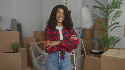 African american woman wearing a red flannel shirt crosses her arms amid stacked cardboard boxes in a modern office building; denial.