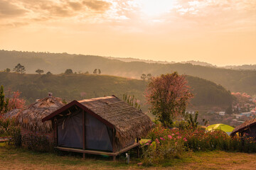 Rustic thatched hut with flower garden blooming overlooking mountain valley in the sunset at Ban Rong Kla, Loei