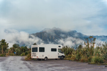 White large motorhome parked on asphalt road with foggy mountain in the forest at New Zealand