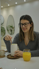 Woman enjoying coffee in a modern luxurious restaurant with a stylish interior and sipping a warm beverage while holding a large cup beside a glass of orange juice.