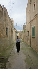 Woman strolling blissfully in a scenic old town alley of mallorca, surrounded by rustic mediterranean architecture and vibrant energy, embracing the charm of this historic environment.