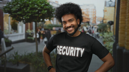 Smiling african american man in security uniform posing outdoors on a bustling city street with...