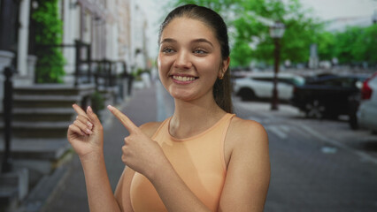 Caucasian teenage girl smiling and pointing fingers along street lined with parked cars; youthful...