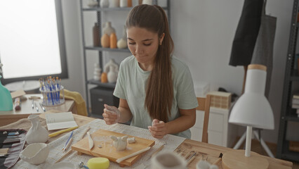 Teenage girl sculpts a clay vase with her hands on a wooden workbench surrounded by sculpting tools in a studio; creativity.