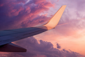 View of the wing of a flying airplane in the purple clouds of the setting sun