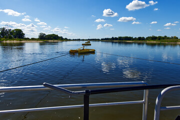 Yellow cable ferry navigating elbe river under bright blue sky, white clouds drifting overhead