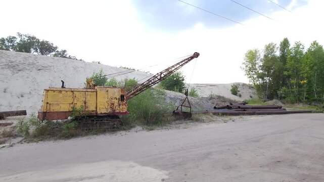 An old dragline in front of a huge mound of sand washed up by a dredger and steel pipes
