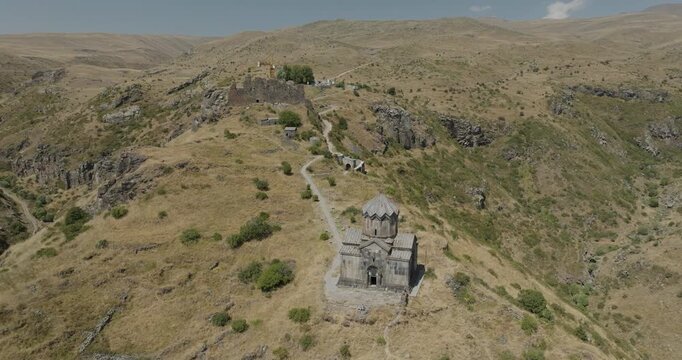 Aerial view of a stone church standing proudly atop a hill, blending with the arid landscape under a clear sky, Mount Aragats, Shirak Province, Armenia.