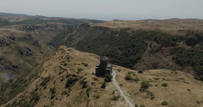 Aerial view of the ancient Saghmosavank Monastery perched upon a cliff, contrasting against the rugged terrain and deep gorge, Mount Aragats, Shirak Province, Armenia.