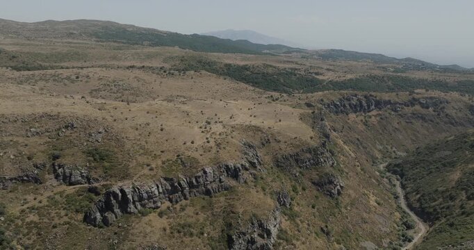 Aerial view of the rugged landscape of Mount Aragats, with its steep cliffs and sparse vegetation, creating a stark contrast against the clear sky, Mount Aragats, Shirak Province, Armenia.