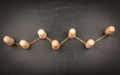 Creative representation of data analysis and statistics using wooden figures connected by a zigzag line symbolizing a graph on a dark chalkboard background