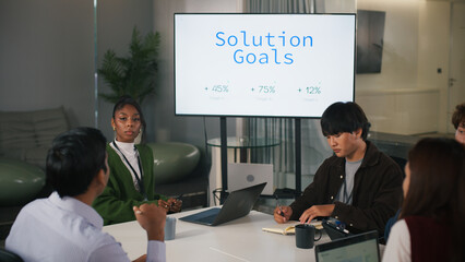 Diverse office teamwork meeting in modern startup workspace with professionals discussing solution goals and growth targets, showing focus and collaboration around digital screen