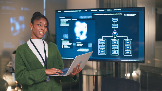 Diverse office teamwork in startup environment with confident woman presenting data analysis on screen using laptop showing innovation and collaboration