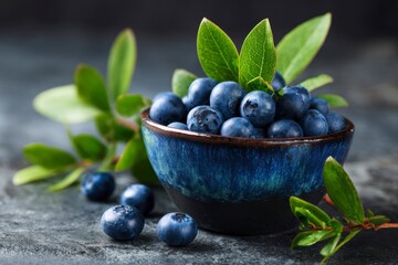 Blueberries fill a blue ceramic bowl accented with green leaves set on a textured dark surface